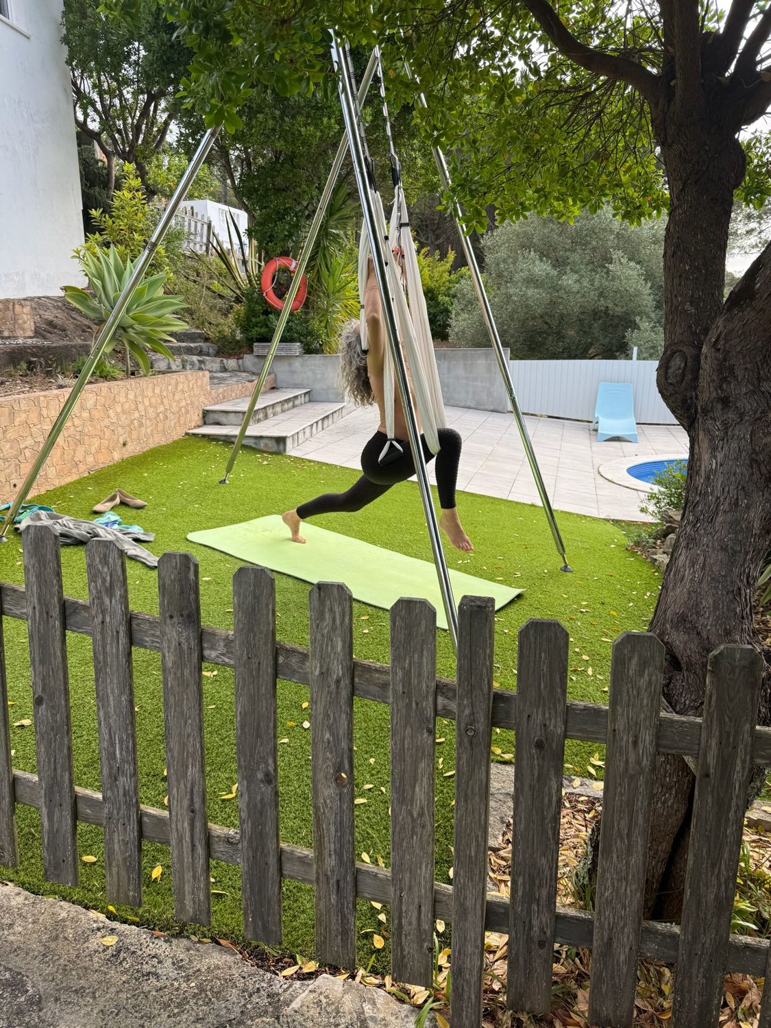 Prática de yoga aéreo num jardim, com o tecido suspenso numa estrutura própria