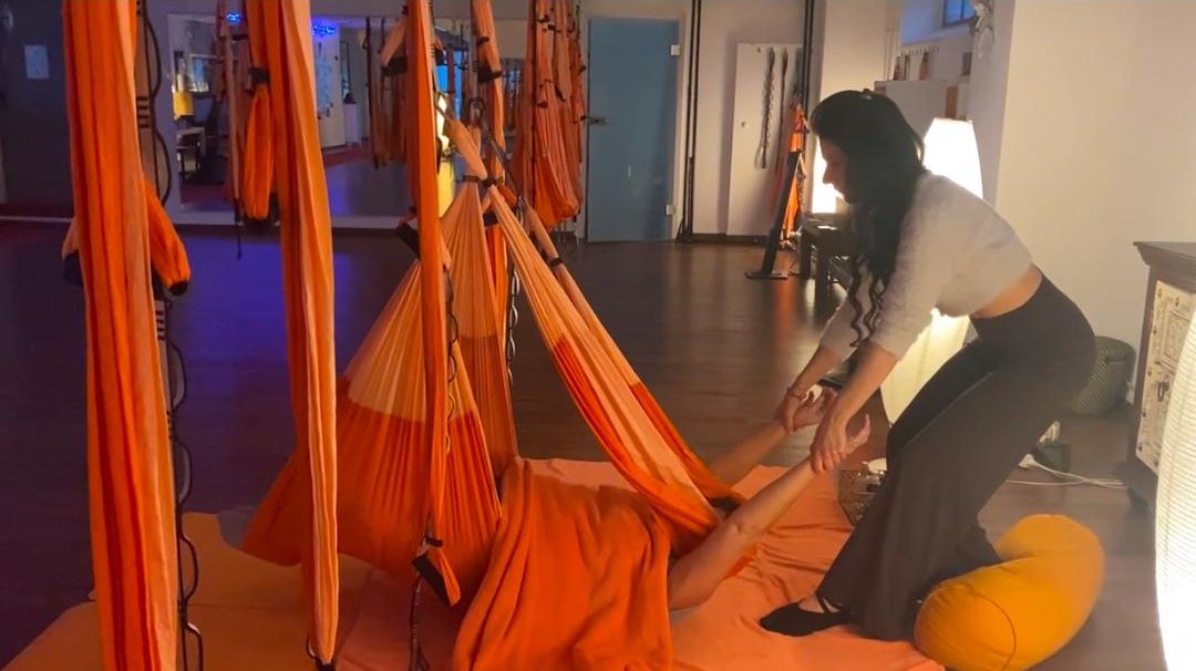 Sessão individual: a professora acompanha os braços de uma pessoa deitada no tecido laranja